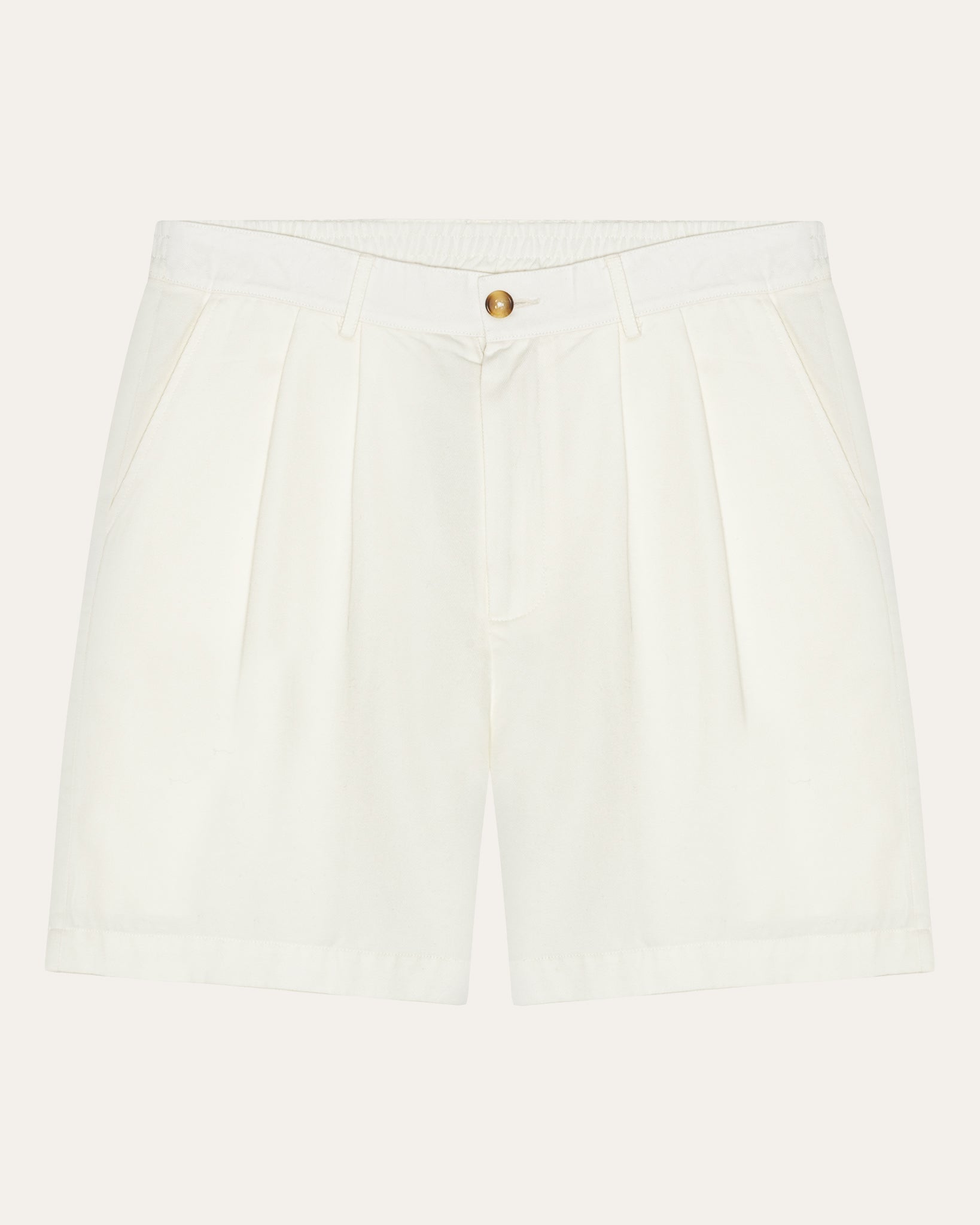 A pair of pleated tennis shorts in warm white color with a relaxed fit and above-the-knee cut. The shorts have a partially elasticated waistband, buttoned back pocket, and extra large front pockets.