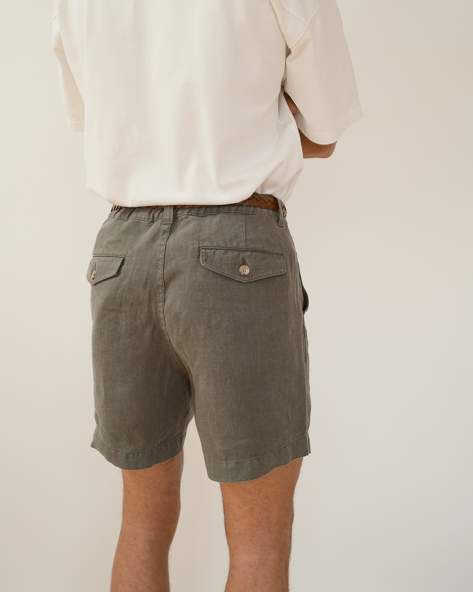 A person viewed from the back wearing olive green shorts with flap pockets and a white shirt, against a plain light background.