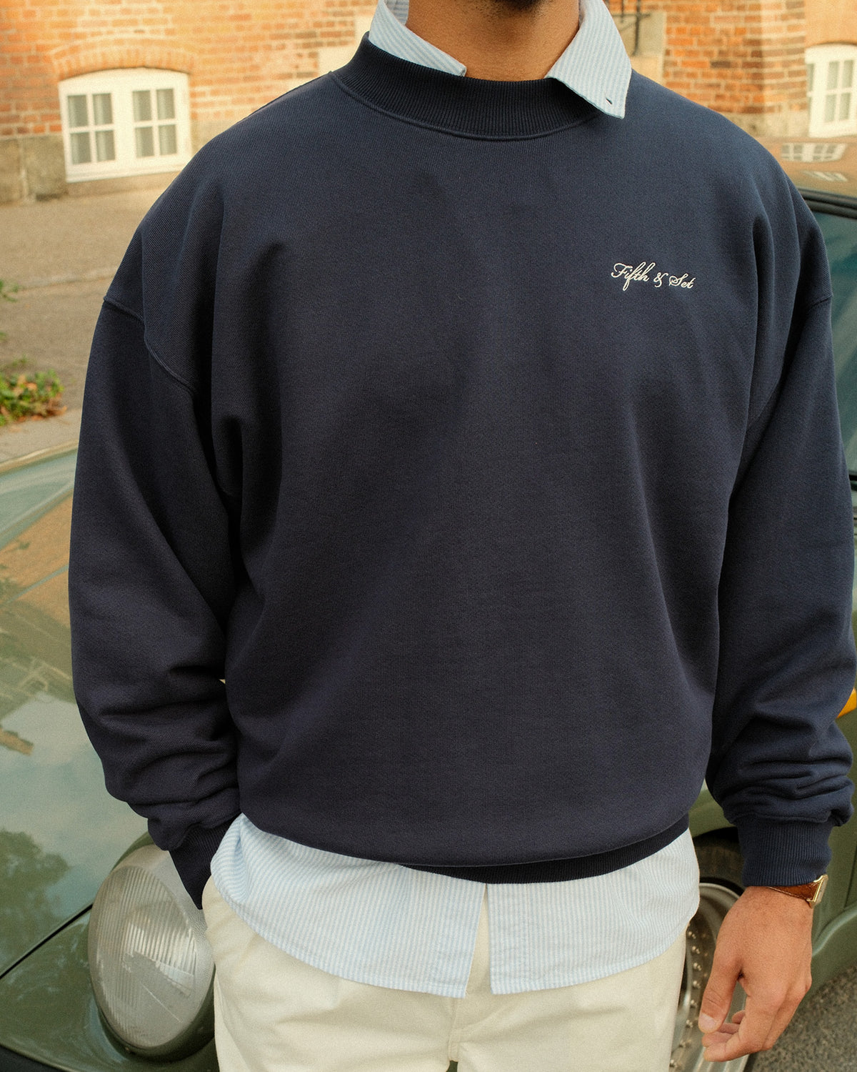 man standing in front of a car wearing a navy sweatshirt with white script embroidery