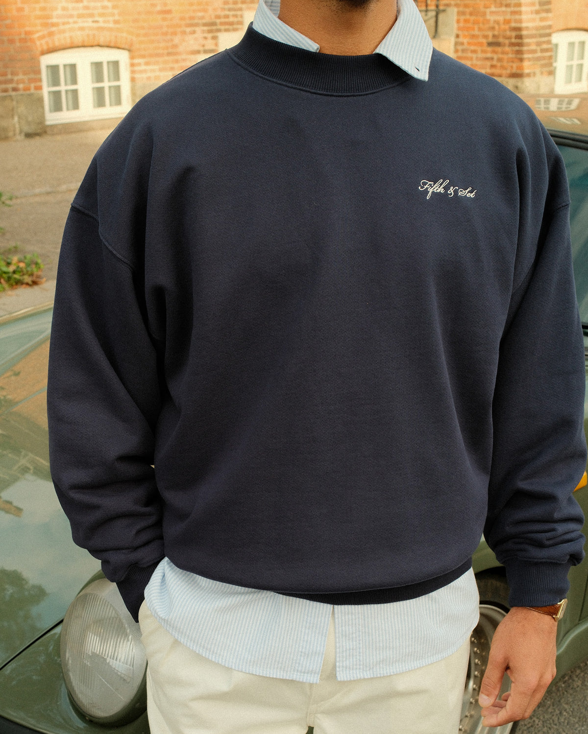 man standing in front of a car wearing a navy sweatshirt with white script embroidery
