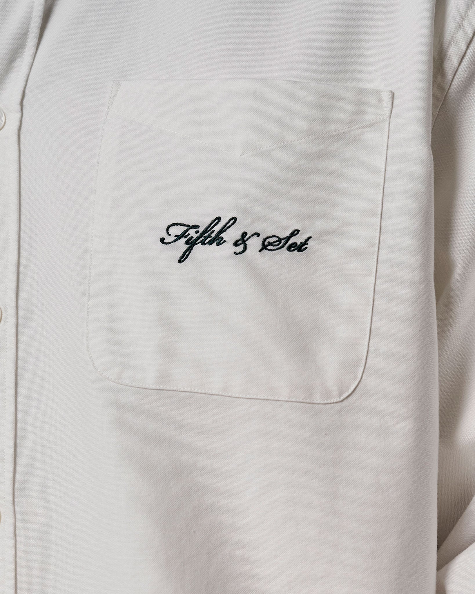 Dark green embroidered logo on pocket of a white men's shirt