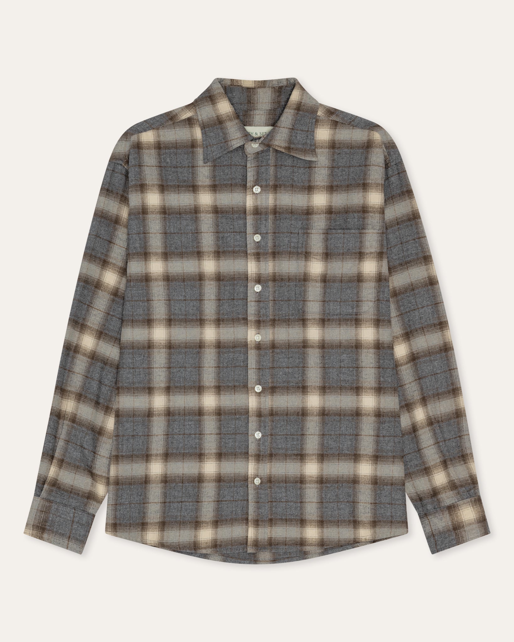 A long-sleeve button-up plaid shirt in gray, beige, and brown tones, laid flat against a light cream background.