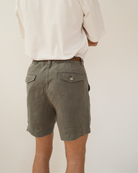 A person viewed from the back wearing olive green shorts with flap pockets and a white shirt, against a plain light background.