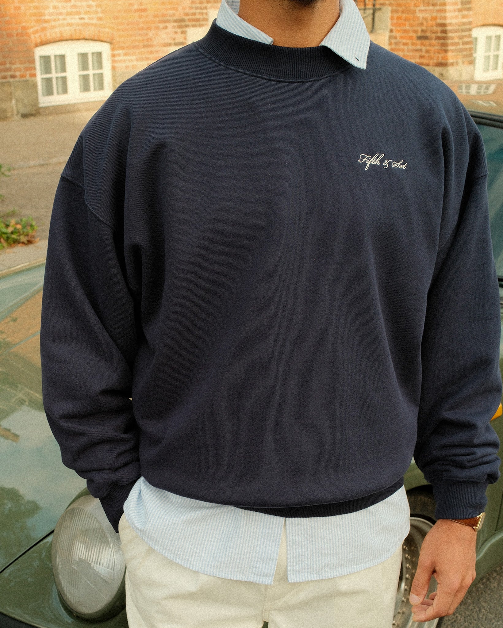 man standing in front of a car wearing a navy sweatshirt with white script embroidery