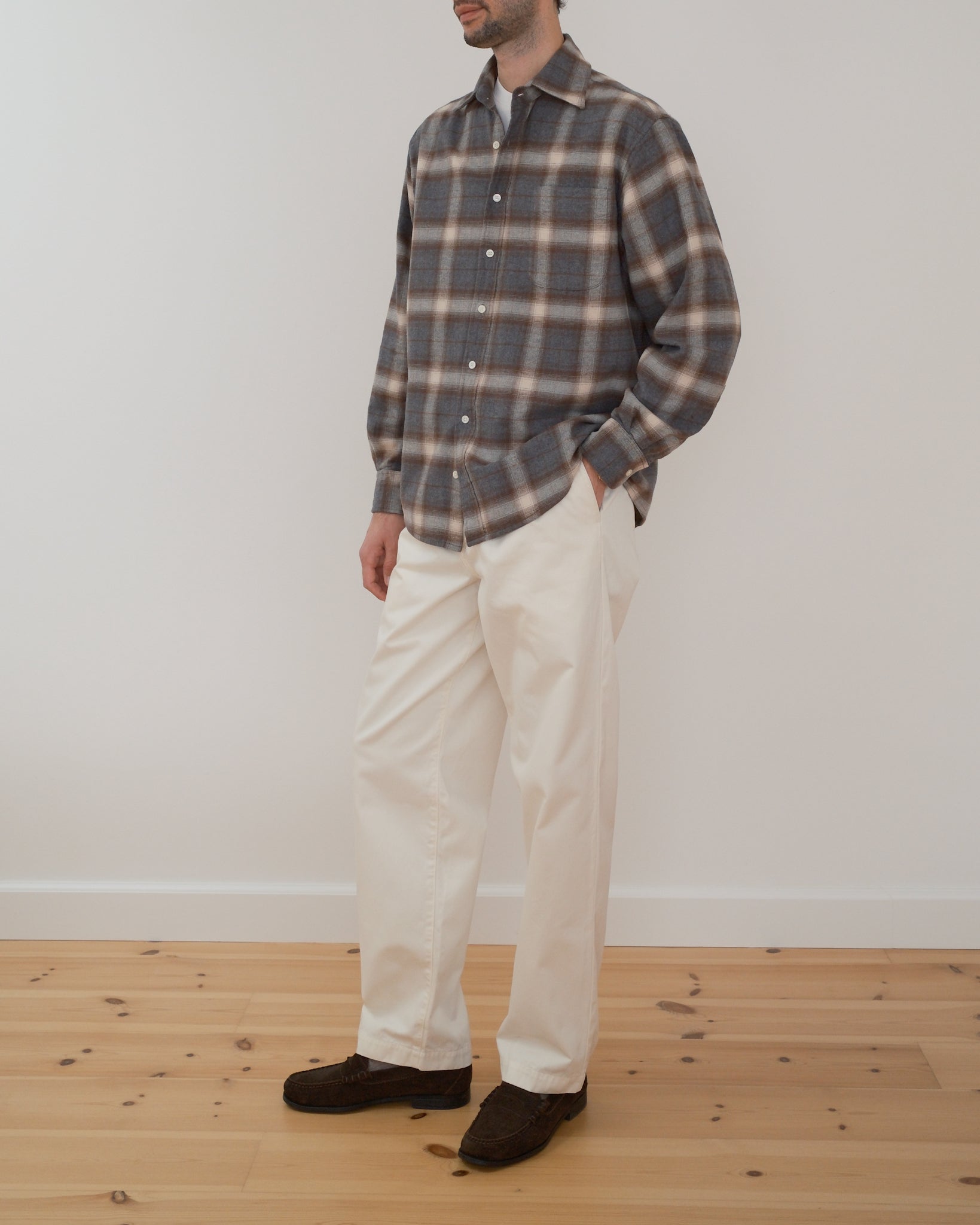 Model wearing a grey, brown and cream checkered flannel shirt in front of a white wall