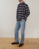Model wearing a navy and cream checkered flannel shirt in front of a white wall