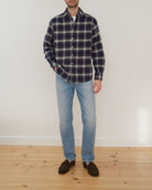 Model wearing a navy and cream checkered flannel shirt in front of a white wall