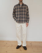 Model wearing a grey, brown and cream checkered flannel shirt in front of a white wall