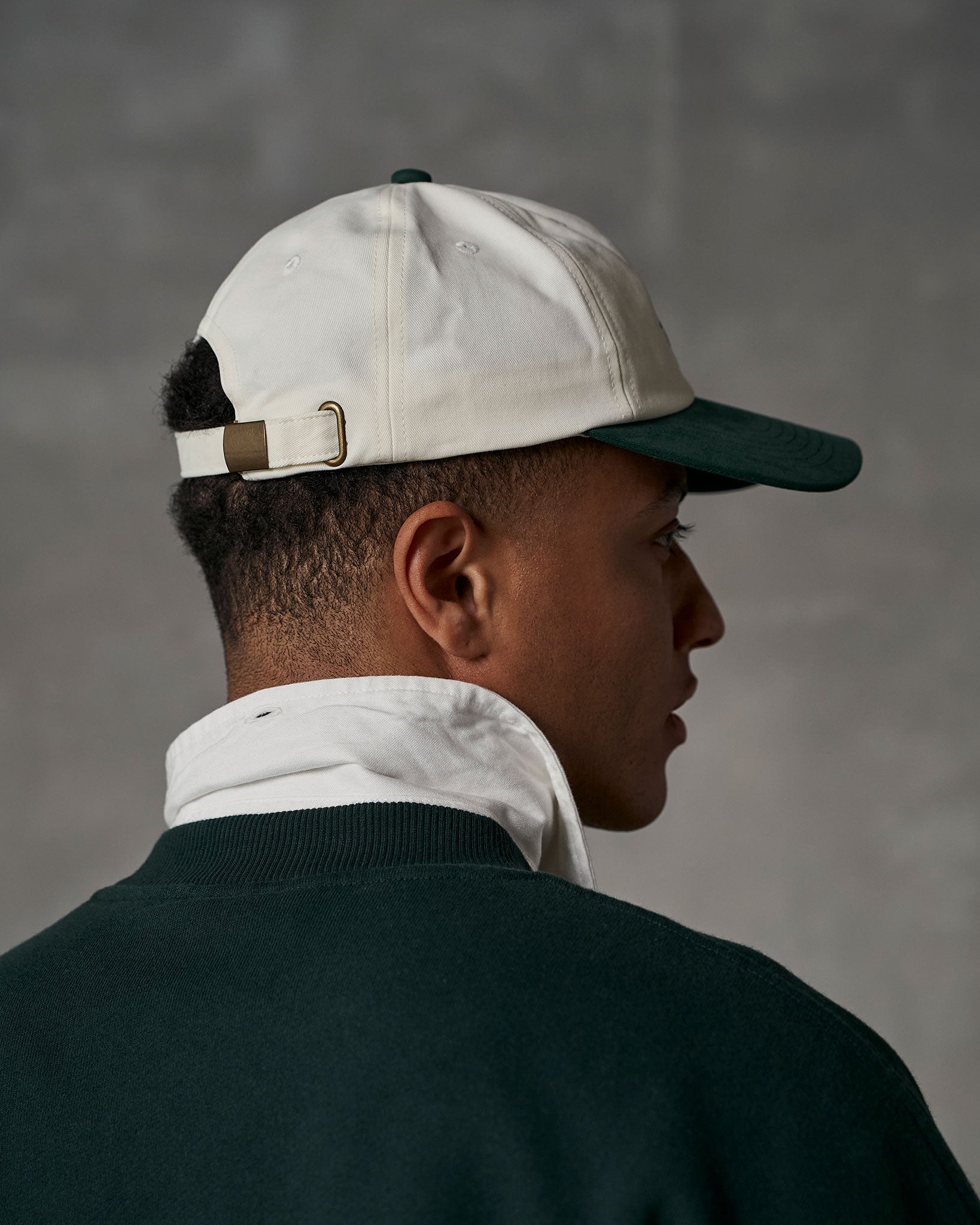 Model wearing two toned cap and dark green sweatshirt.